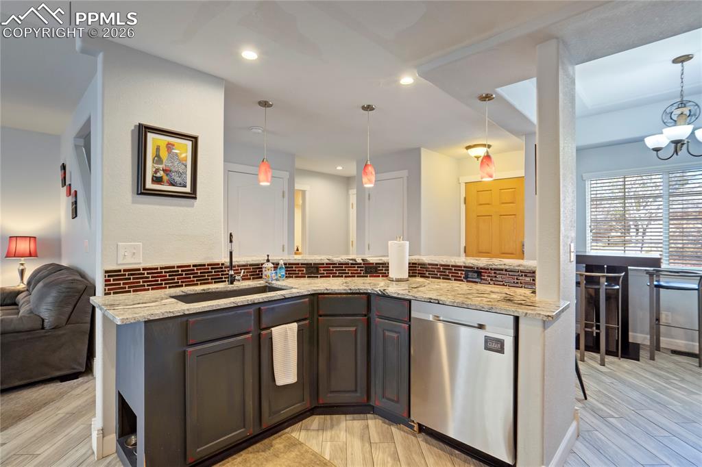 Kitchen with open floor plan, dishwasher, backsplash, light wood finished floors, and light stone counters