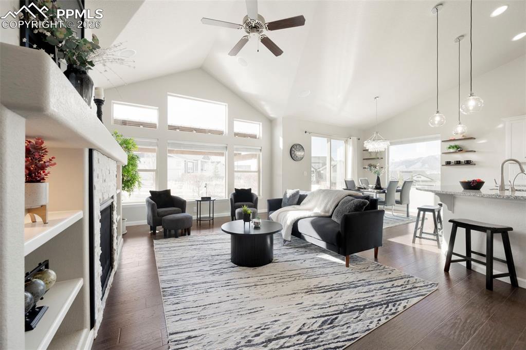 Living room featuring dark wood-style floors, a high ceiling, a stone fireplace, a ceiling fan, and recessed lighting