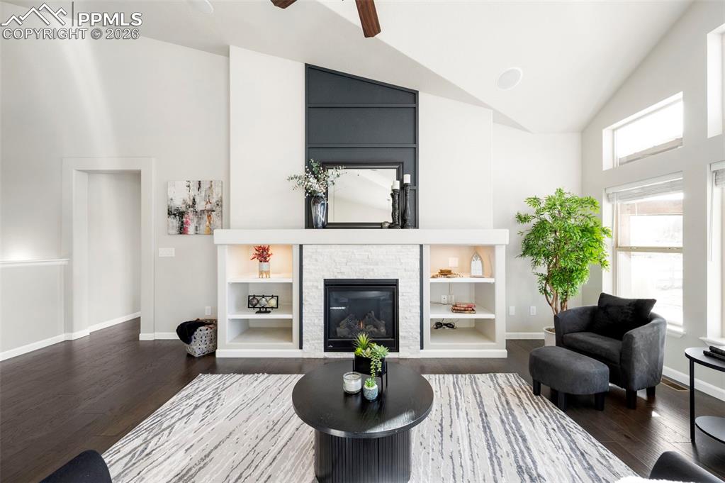 Living room with vaulted ceiling, dark wood-type flooring, built in shelves, a fireplace, and a ceiling fan