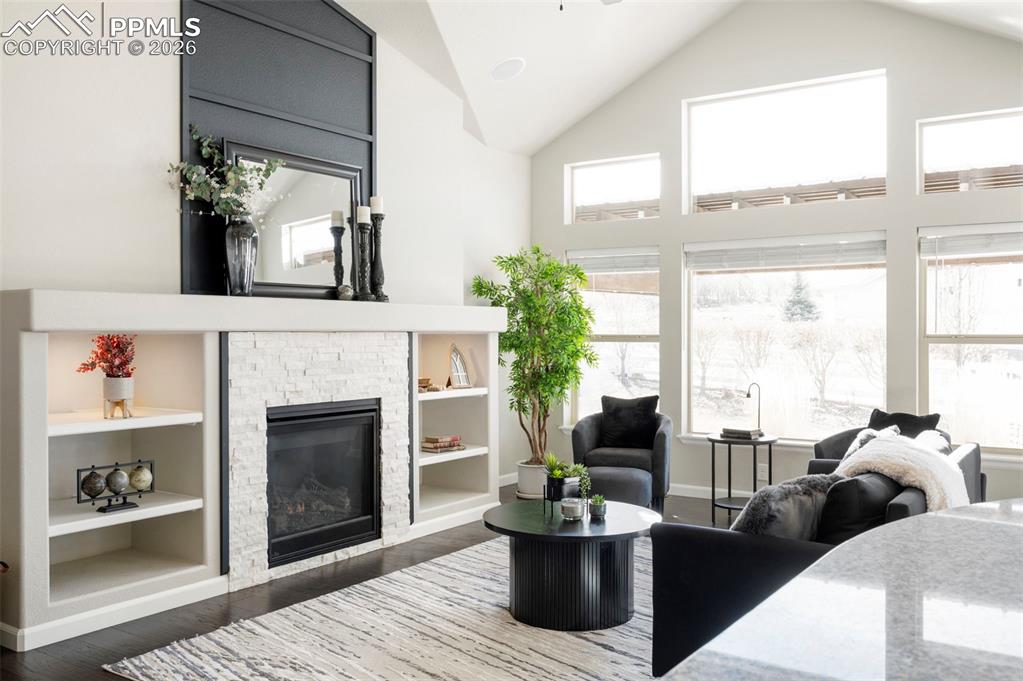 Living room featuring a high ceiling, a fireplace, dark wood-type flooring, built in shelves, and ceiling fan