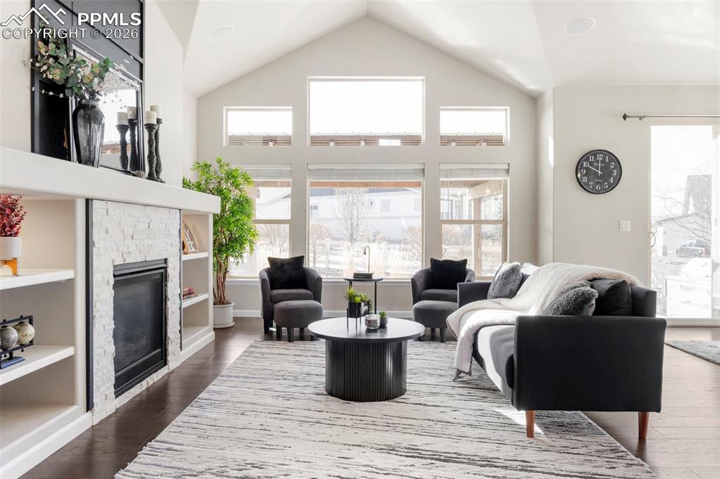 Living area featuring a high ceiling, a fireplace, dark wood-type flooring, and built in shelves