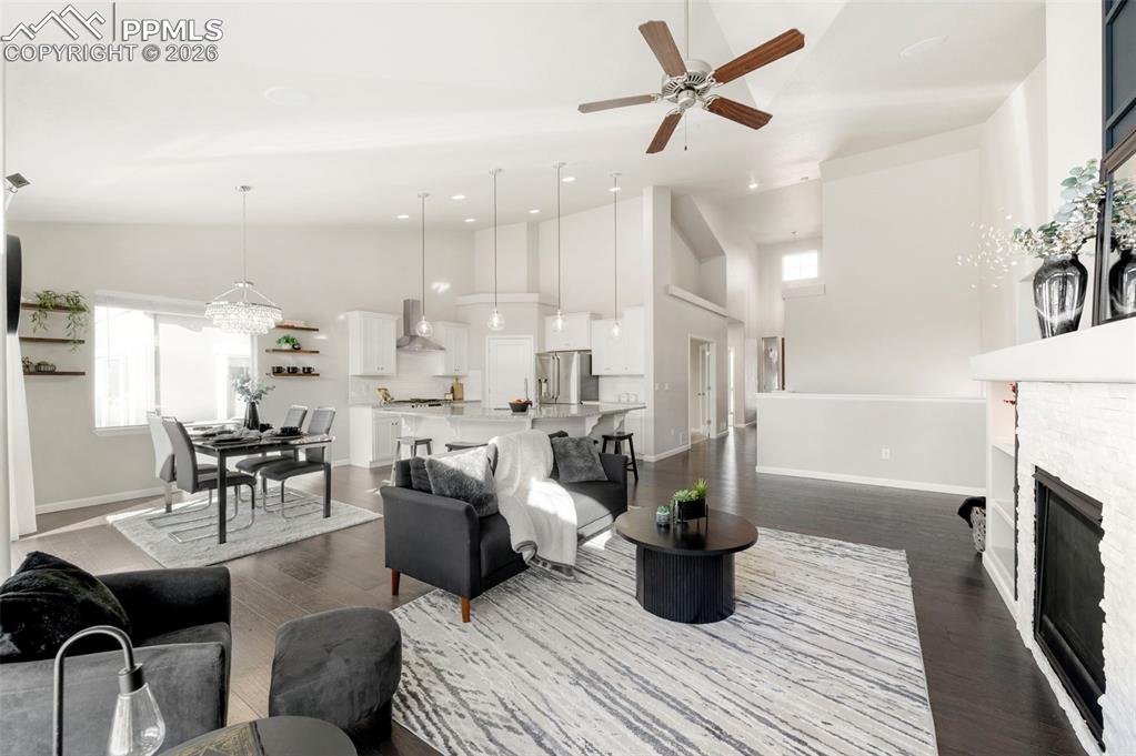 Living area featuring a fireplace, a ceiling fan, dark wood finished floors, vaulted ceiling, and suspended lighting