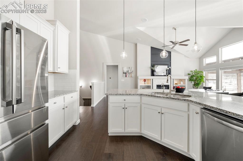 Kitchen featuring stainless steel appliances, white cabinets, dark wood-style flooring, light stone countertops, and a ceiling fan