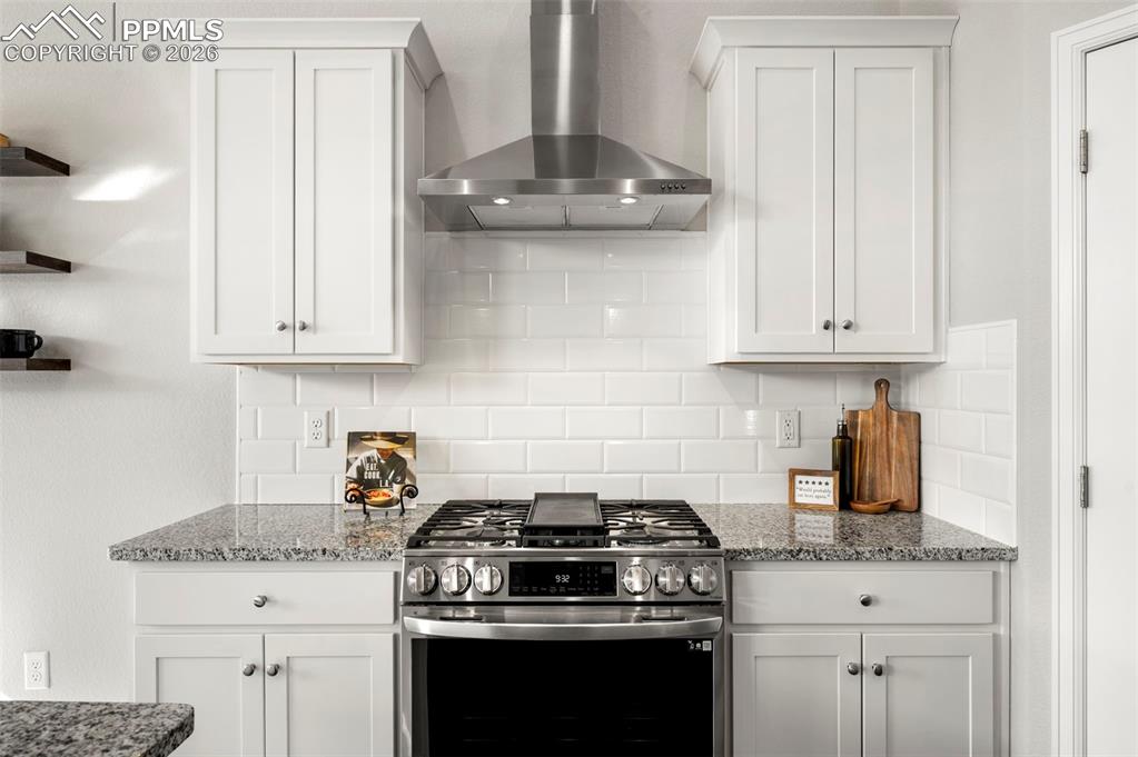 Kitchen with stainless steel gas stove, white cabinetry, light stone countertops, open shelves, and backsplash