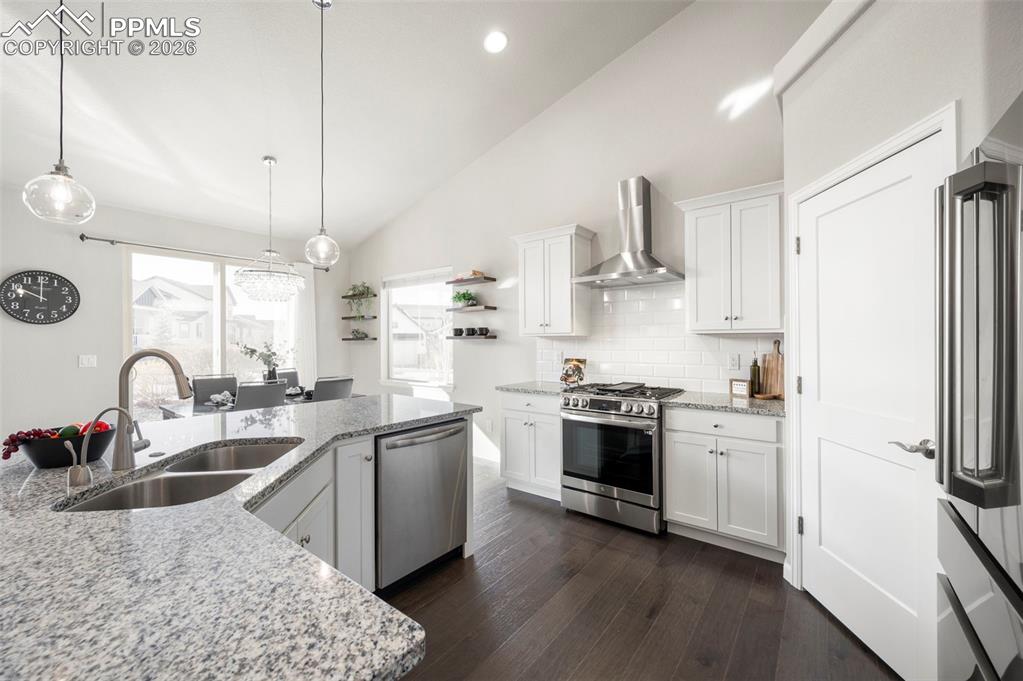 Kitchen with stainless steel appliances, white cabinets, lofted ceiling, dark wood finished floors, and light stone counters