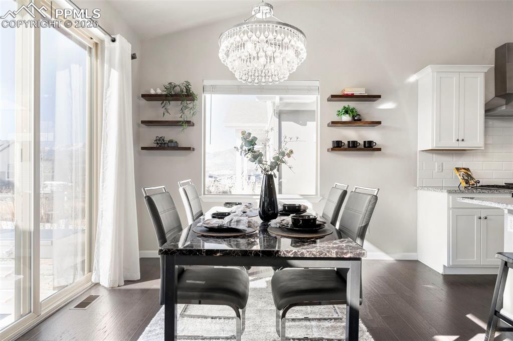 Dining area with dark wood finished floors, suspended lighting, plenty of natural light, and lofted ceiling