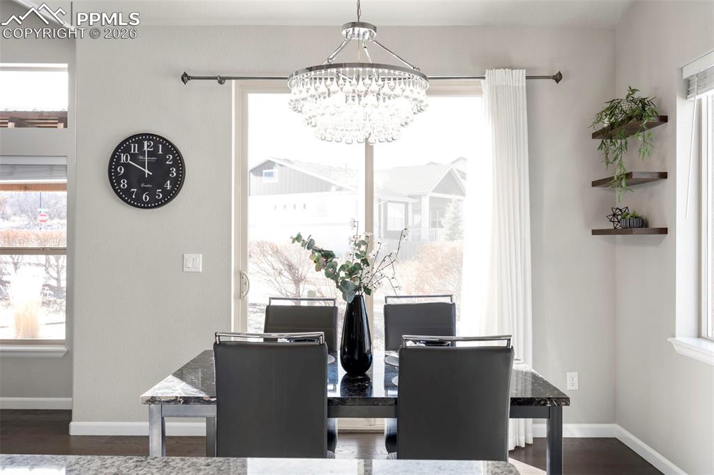 Dining room with dark wood finished floors, hanging lights, and plenty of natural light