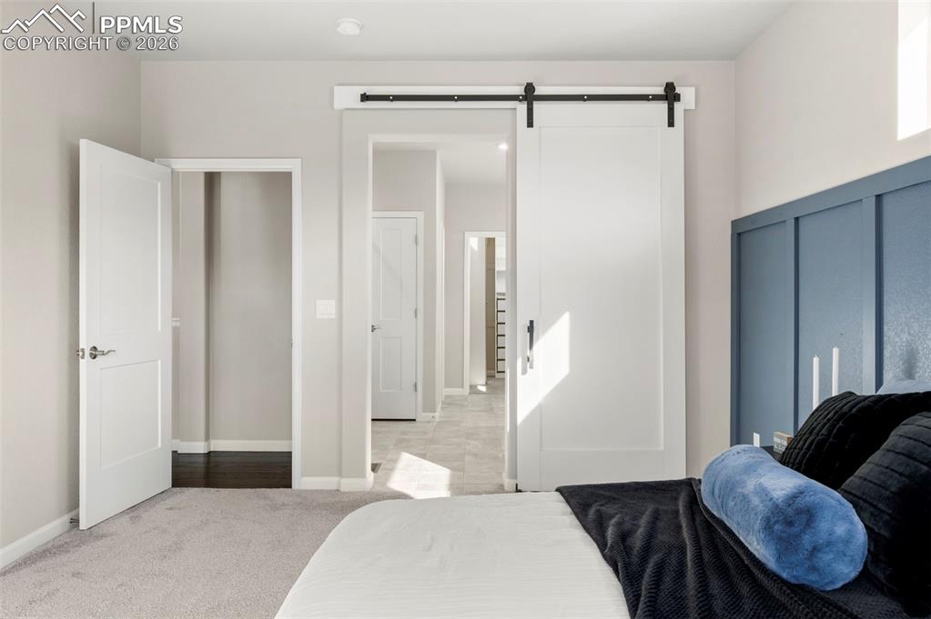 Bedroom with a barn door, light colored carpet, and a decorative wall