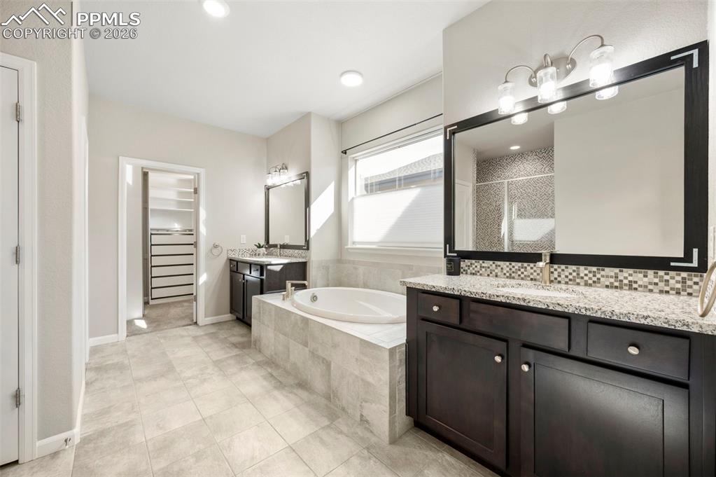 Bathroom featuring a spacious closet, a garden tub, two vanities, a shower stall, and light tile patterned flooring