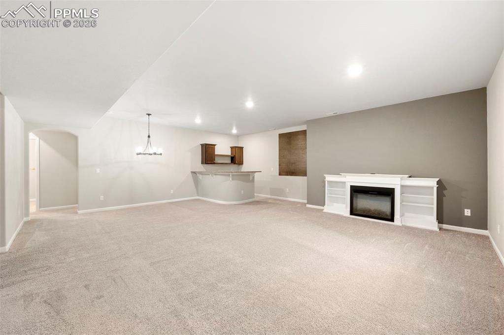 Unfurnished living room featuring light colored carpet, a glass covered fireplace, and a chandelier