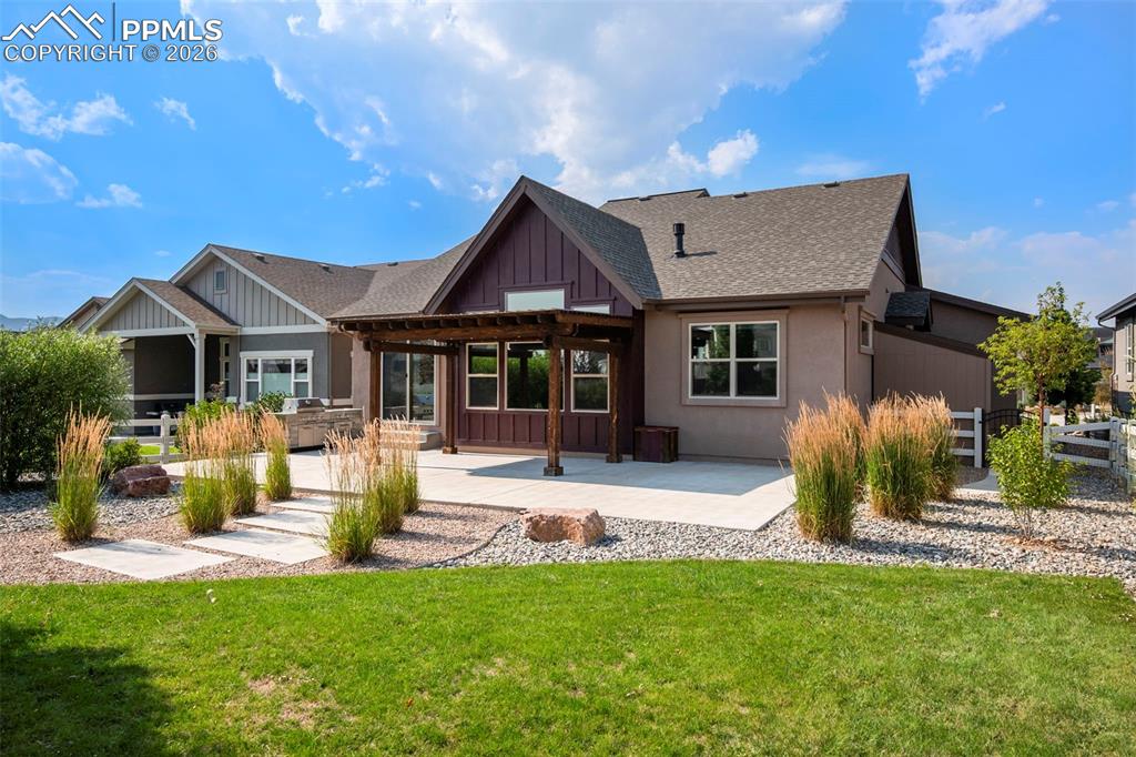 Rear view of property featuring board and batten siding, a patio, roof with shingles, and a lawn