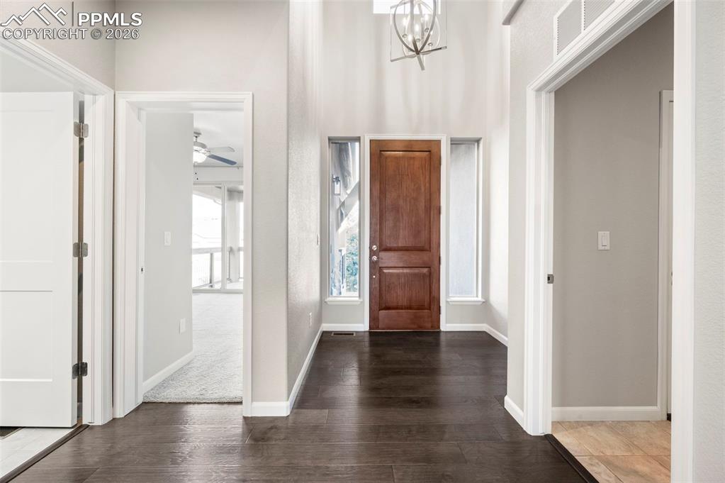 Foyer entrance featuring wood finished floors, hanging lights, a ceiling fan, and a high ceiling