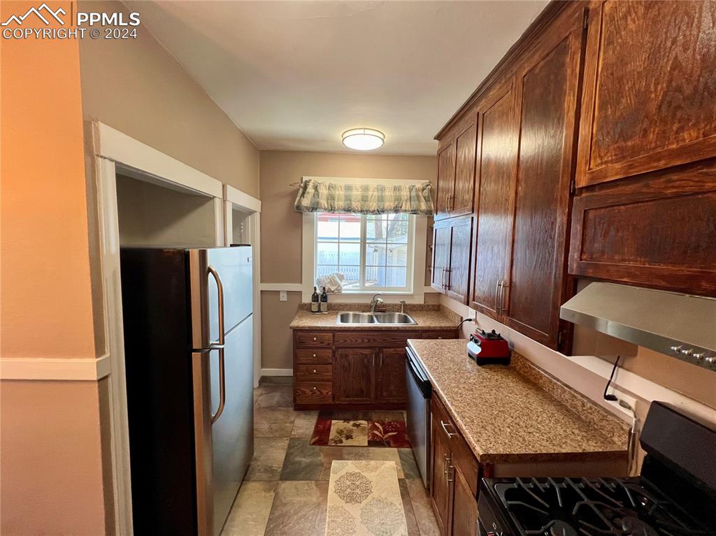 Kitchen with appliances with stainless steel finishes, sink, light stone countertops, and tile floors