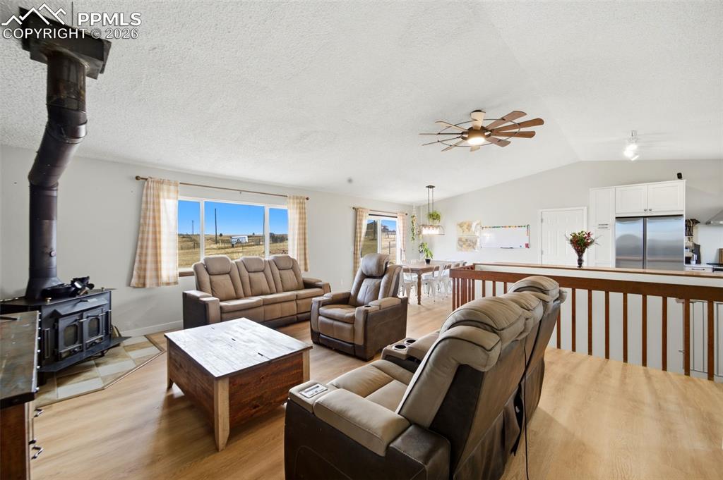 Living room with a wood stove, ceiling fan, light wood finished floors, lofted ceiling, and a textured ceiling