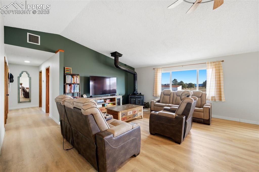 Living area with a wood stove, vaulted ceiling, light wood-type flooring, and a ceiling fan