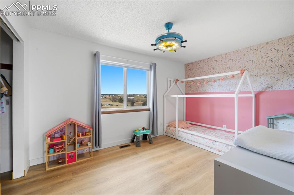 Bedroom with a textured ceiling, light wood-type flooring, and wallpapered walls