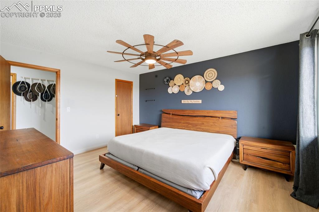 Bedroom with light wood finished floors, ceiling fan, and a textured ceiling