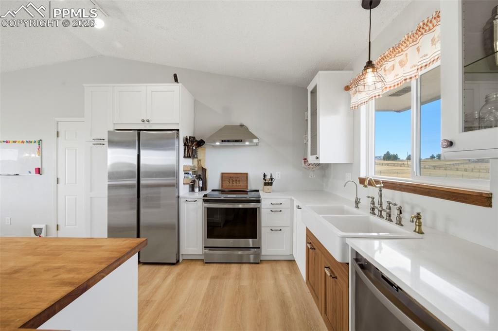 Kitchen featuring glass insert cabinets, white cabinets, appliances with stainless steel finishes, pendant lighting, and lofted ceiling