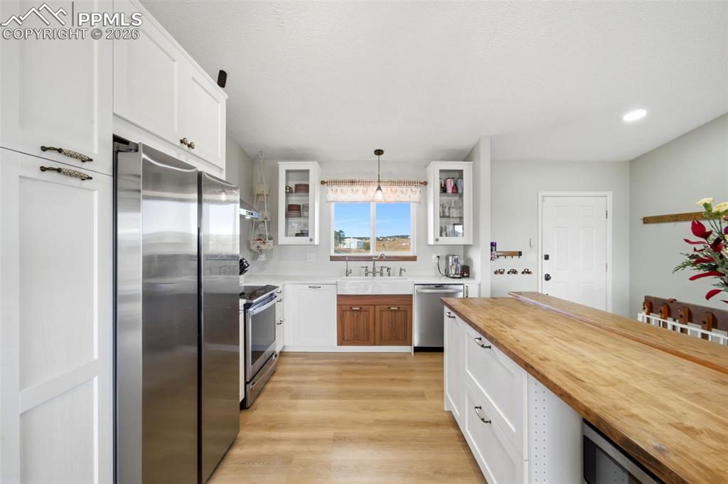 Kitchen featuring white cabinetry, butcher block counters, appliances with stainless steel finishes, glass insert cabinets, and decorative light fixtures