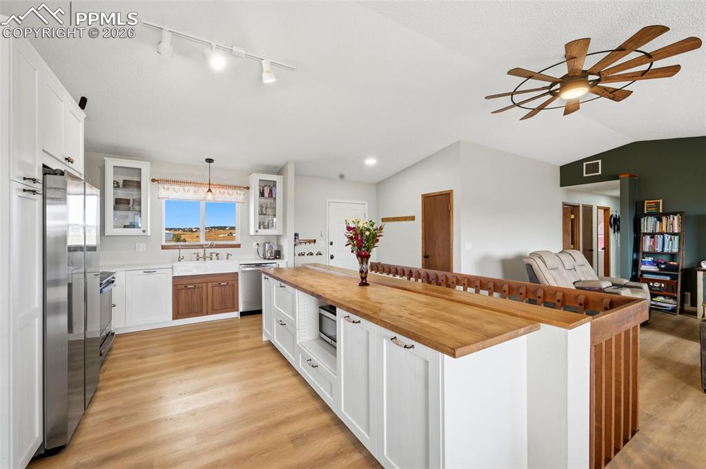 Kitchen with white cabinetry, glass insert cabinets, wooden counters, ceiling fan, and light wood-style flooring