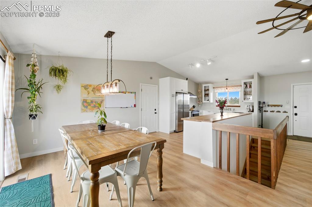 Dining space featuring lofted ceiling, light wood-style floors, a textured ceiling, and a ceiling fan