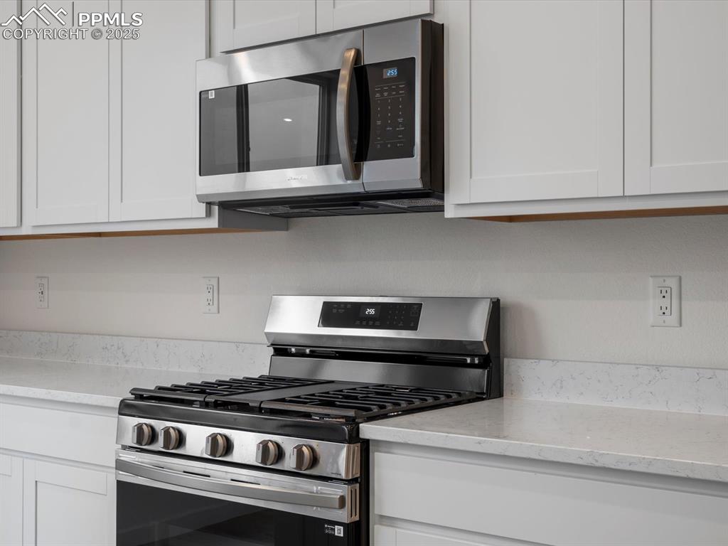 Kitchen with appliances with stainless steel finishes, white cabinets, and light stone countertops