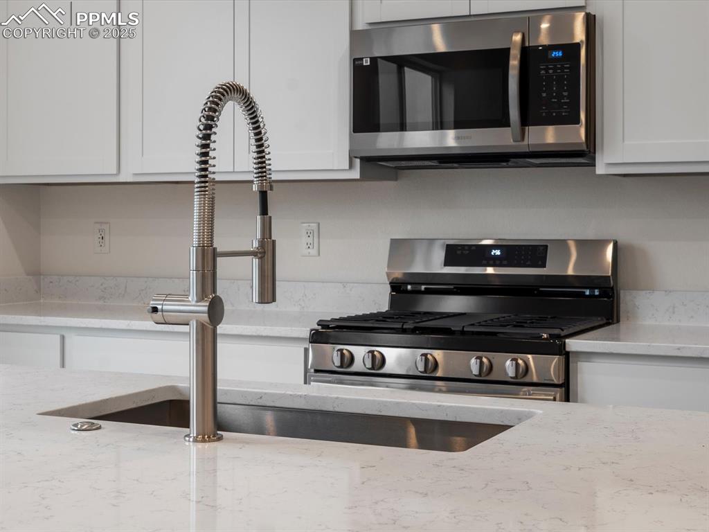 Kitchen featuring appliances with stainless steel finishes, white cabinetry, and light stone counters