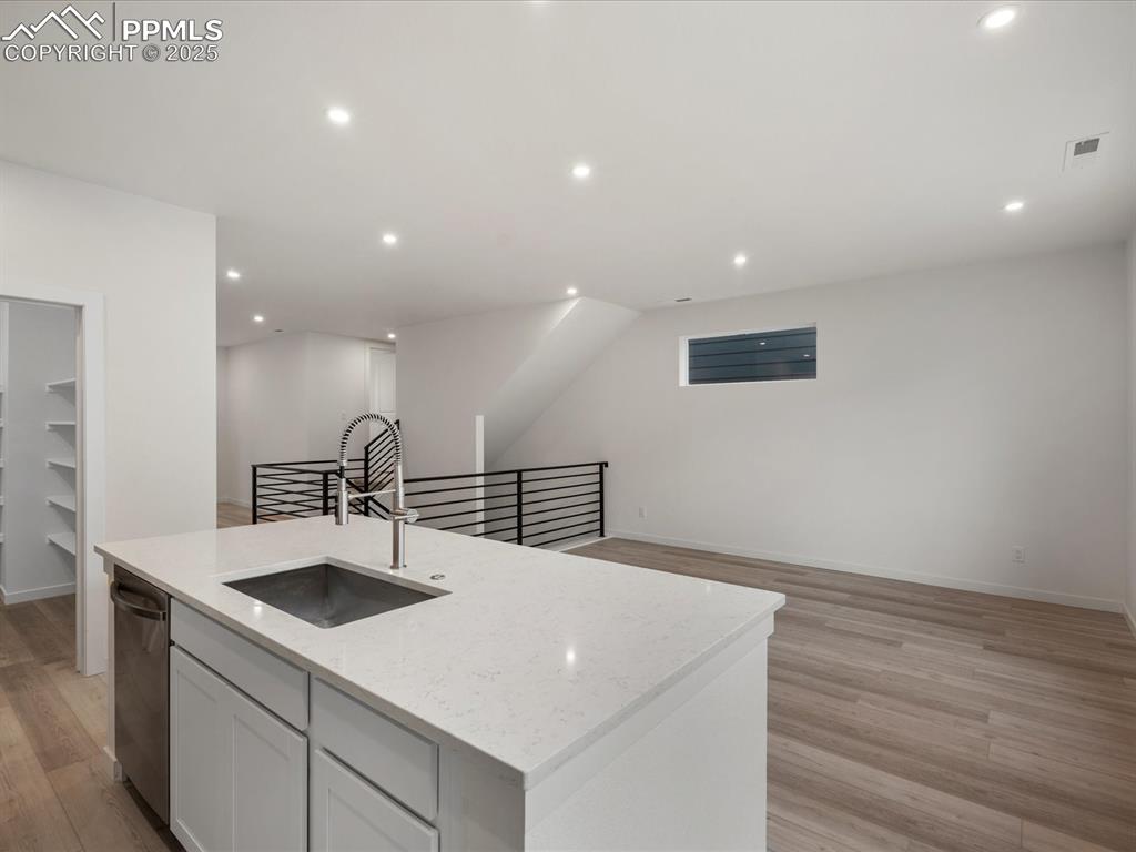 Kitchen featuring open floor plan, a center island with sink, recessed lighting, light wood-type flooring, and light stone counters