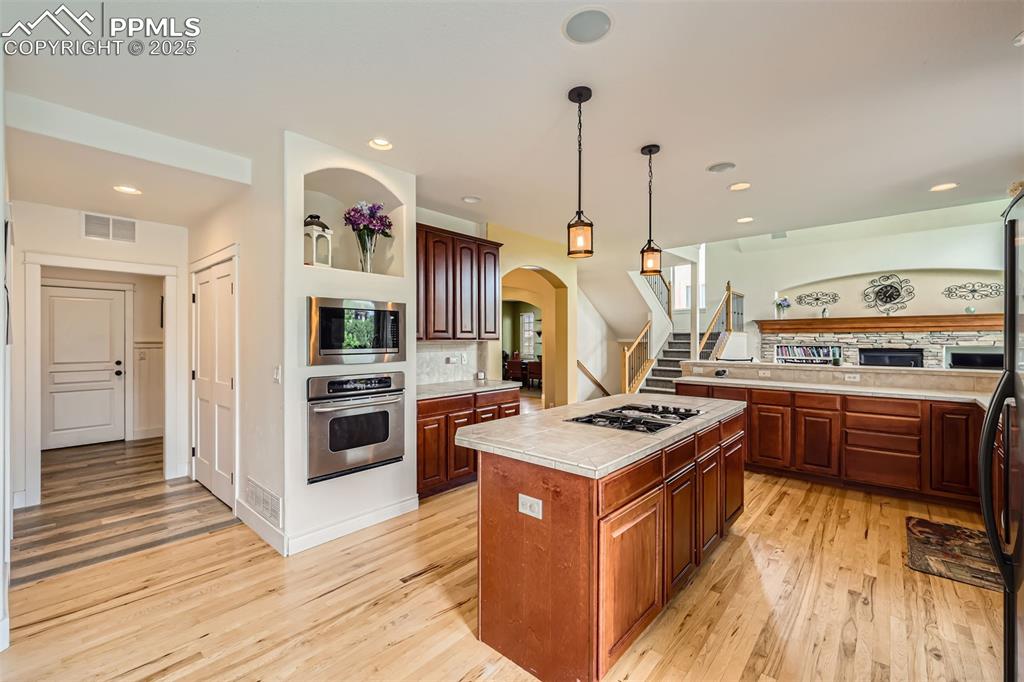 Kitchen with stainless steel appliances, light hardwood floors, arched walkways, a kitchen island, and tile countertops