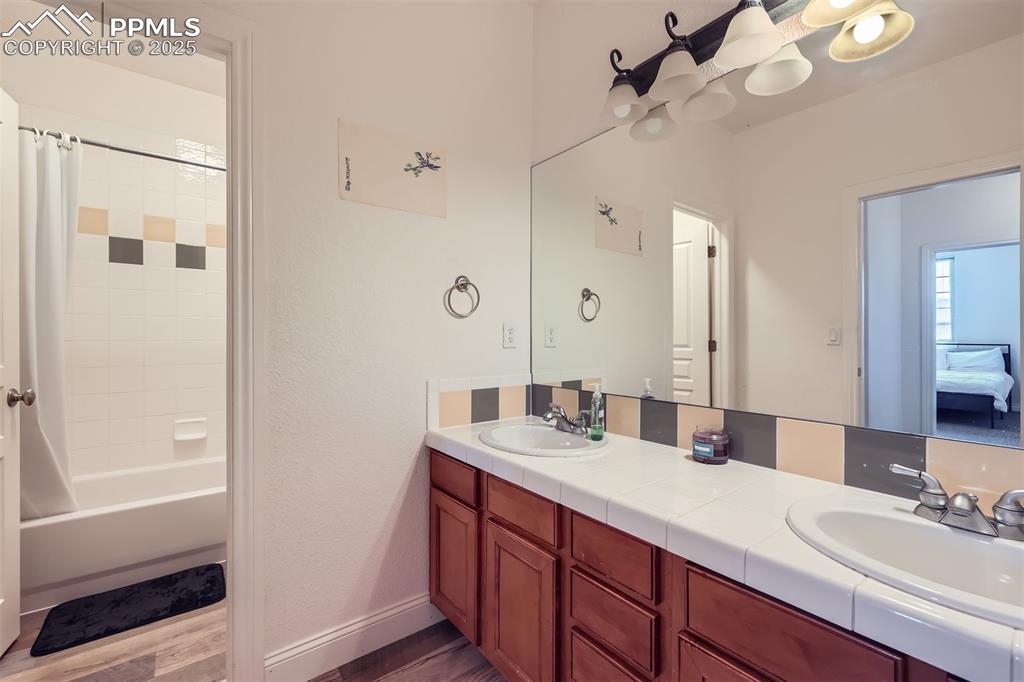 Bathroom with double vanity, shower / tub combo with curtain, and faux wood finished floors