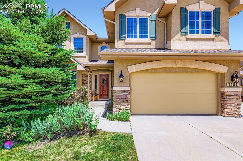 View of front of property featuring driveway, an attached 4-car garage, stone siding, and stucco siding