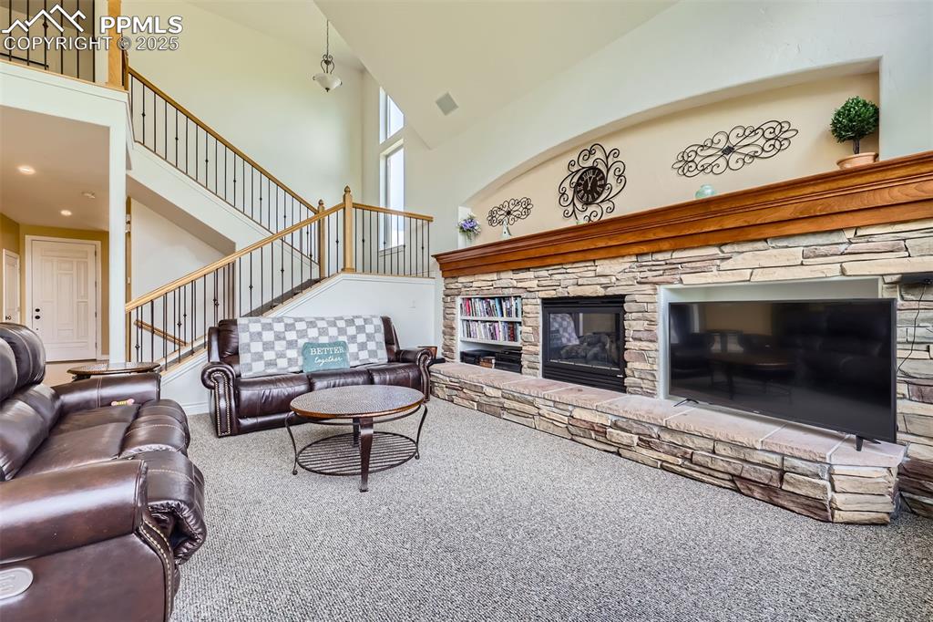 Carpeted living area with a high ceiling, a fireplace, and stairway