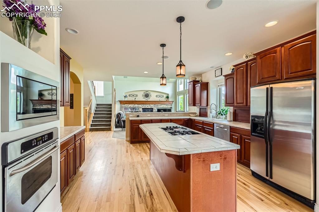 Kitchen featuring appliances with stainless steel finishes, tile countertops, a peninsula, a center island, and light hardwood floors