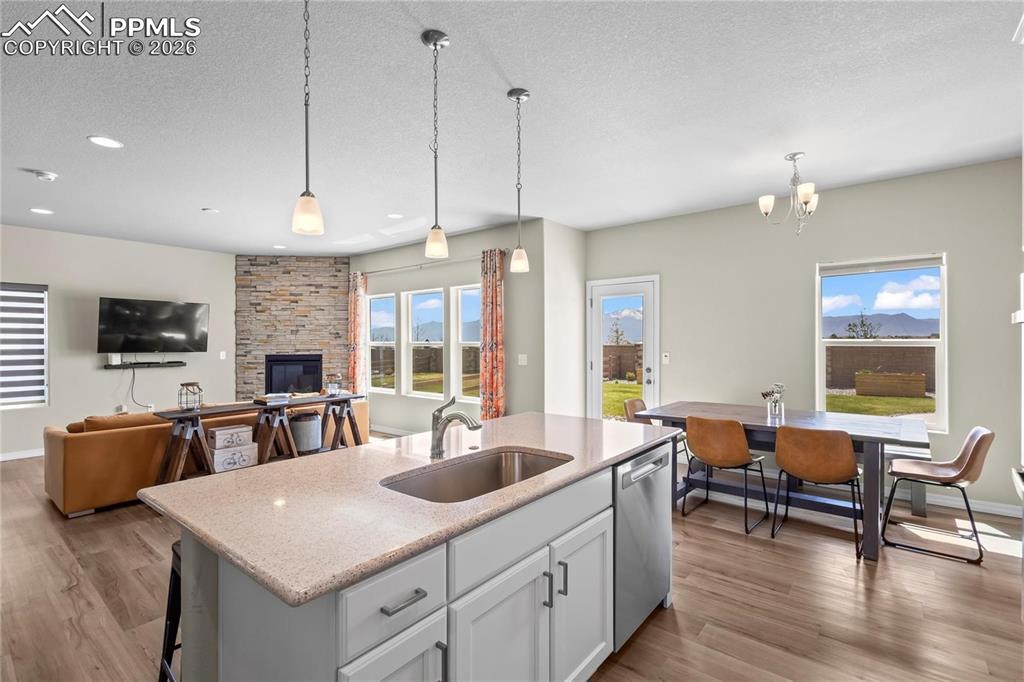 Kitchen featuring open floor plan, a kitchen island with sink, a textured ceiling, light stone counters, and light wood-type flooring