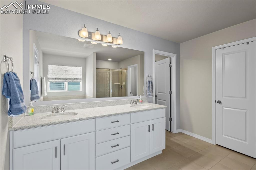 Bathroom featuring double vanity, a stall shower, and light tile patterned floors