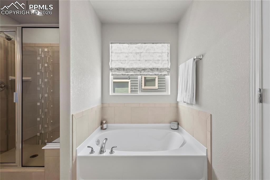 Full bath featuring a stall shower, a garden tub, and a textured wall