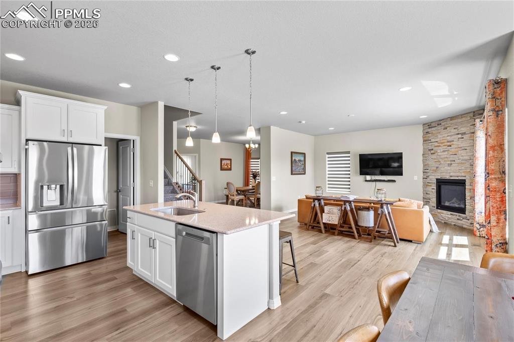 Kitchen featuring open floor plan, white cabinetry, stainless steel appliances, a center island with sink, and light stone counters
