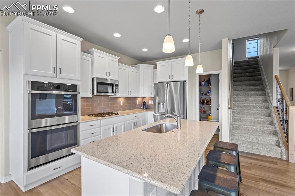 Kitchen featuring stainless steel appliances, white cabinets, light wood finished floors, an island with sink, and a breakfast bar area