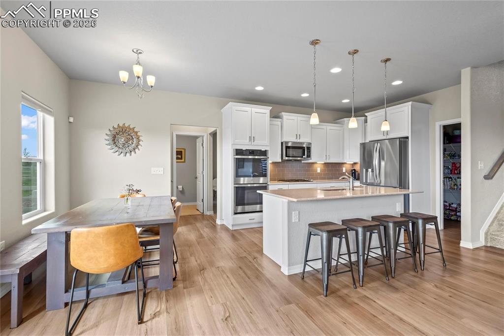 Kitchen featuring a kitchen bar, an island with sink, white cabinetry, a chandelier, and stainless steel appliances