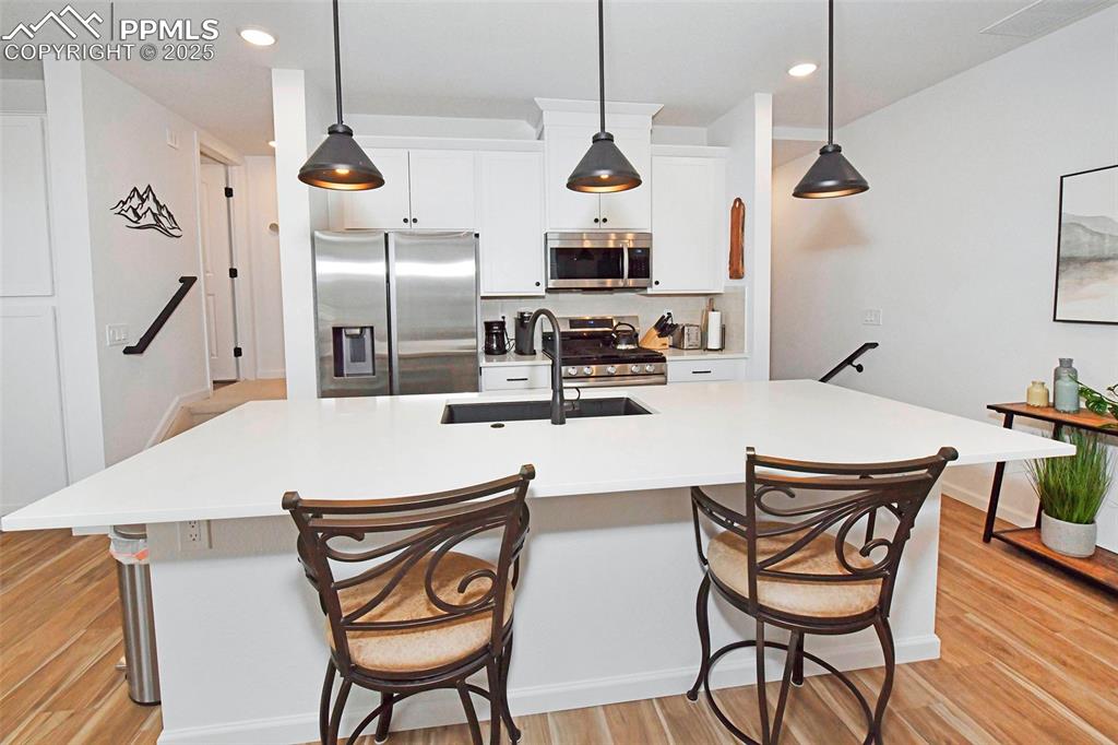 Kitchen featuring stainless steel appliances, decorative light fixtures, a center island with sink, white cabinets, and recessed lighting