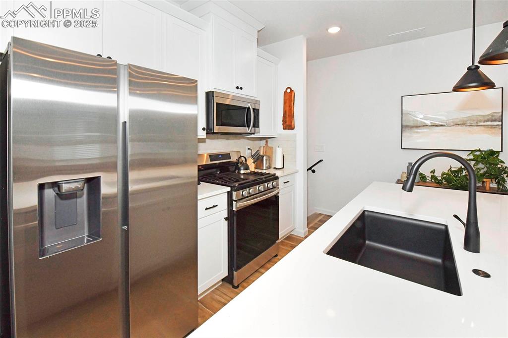 Kitchen with stainless steel appliances, white cabinets, recessed lighting, wood finished floors, and decorative light fixtures