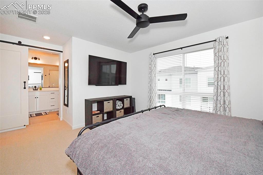 Bedroom featuring a barn door, light carpet, a ceiling fan, recessed lighting, and ensuite bathroom