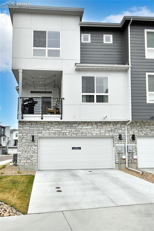 View of front of property with a balcony, a garage, driveway, stone siding, and stucco siding