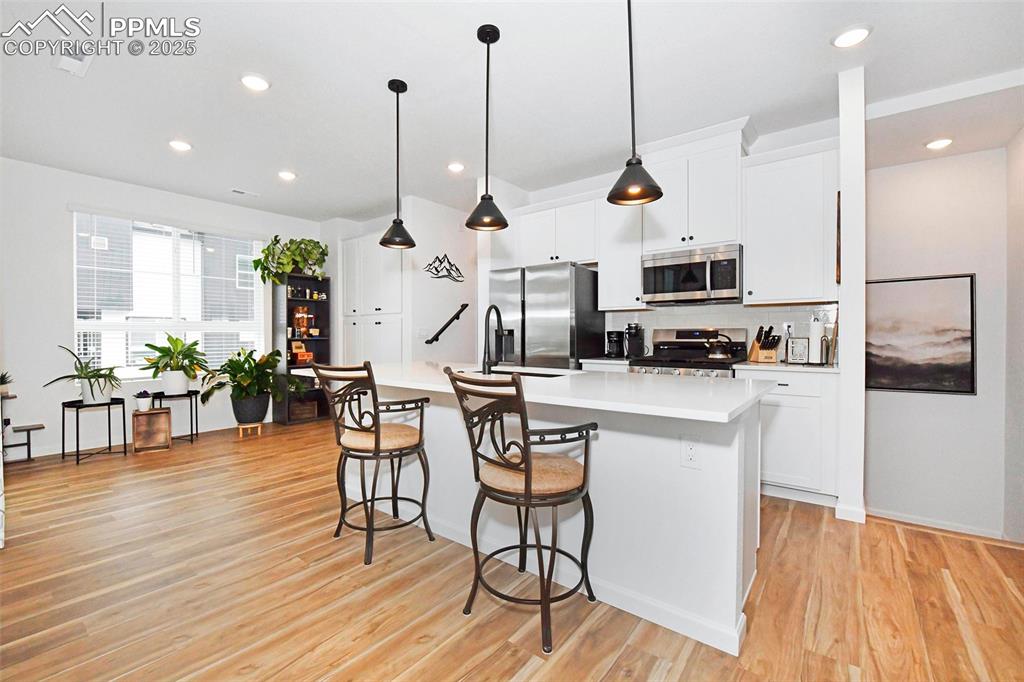 Kitchen with white cabinets, stainless steel appliances, decorative light fixtures, a center island with sink, and a breakfast bar