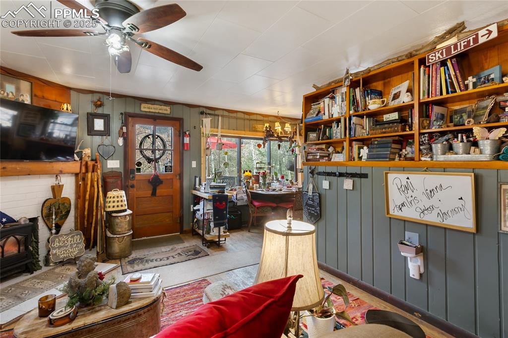 front entry and living area featuring wooden walls, a wood stove, and a ceiling fan