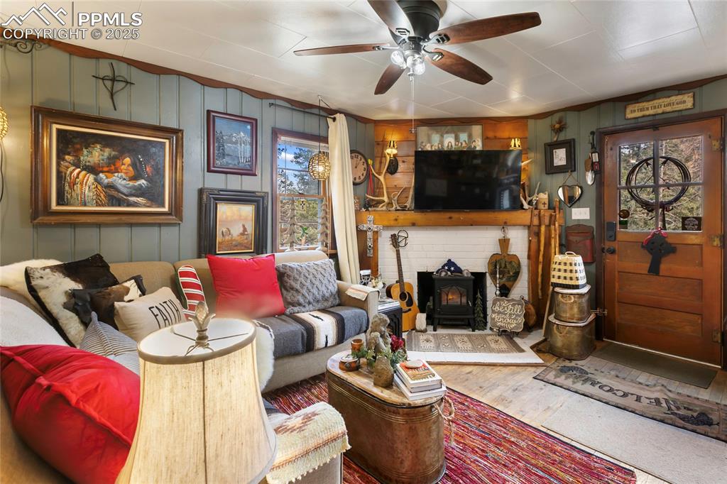 Living area featuring wood walls, healthy amount of natural light, a wood stove, wood finished floors, and a ceiling fan