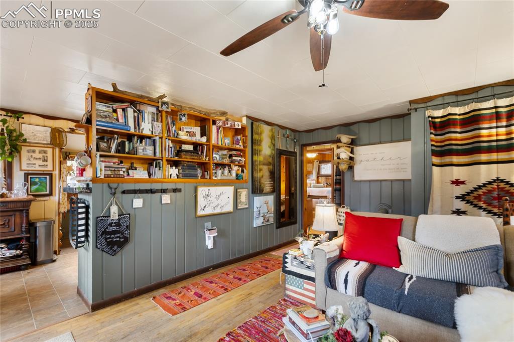 Living room with wood finished floors, wooden walls, and a ceiling fan