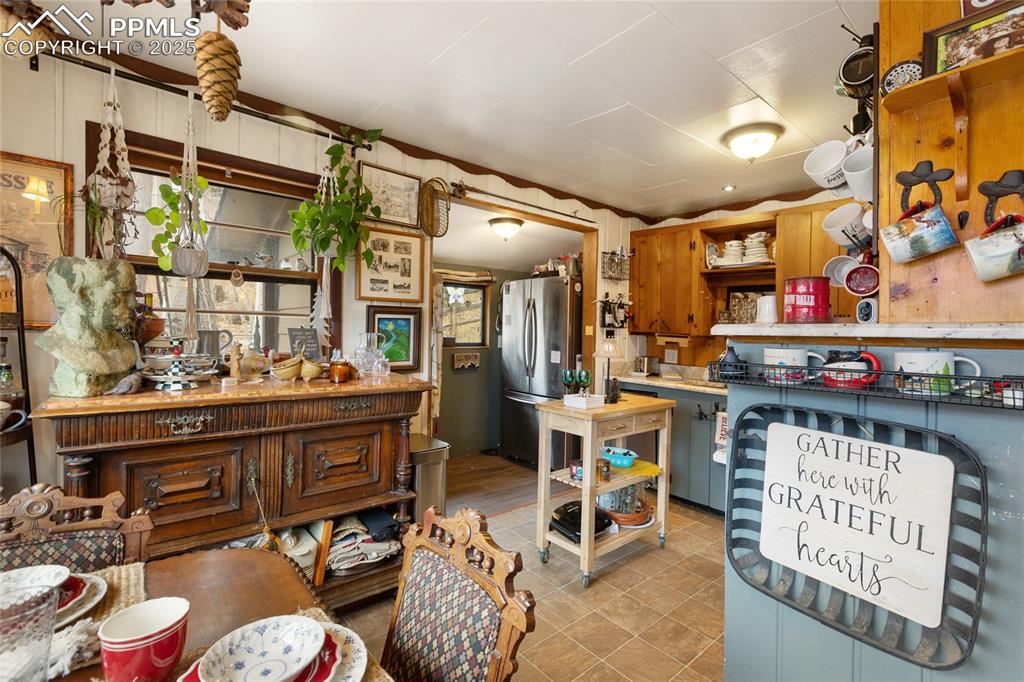 Kitchen with open shelves, freestanding refrigerator, brown cabinets, light tile patterned flooring, and wooden walls