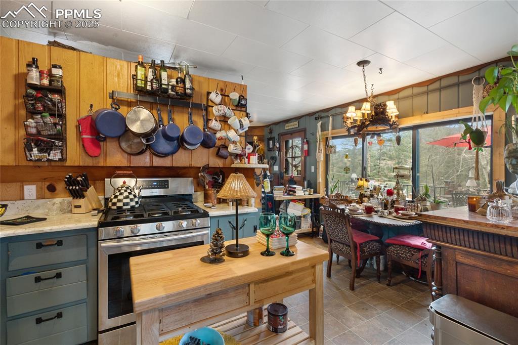 Kitchen featuring stainless steel gas stove, wooden walls, a chandelier, light stone countertops, and pendant lighting