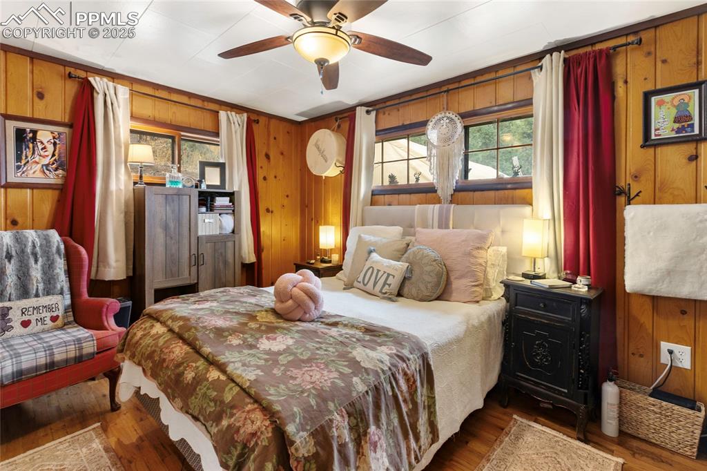 Main Bedroom with wooden walls, wood finished floors, multiple windows, and a ceiling fan